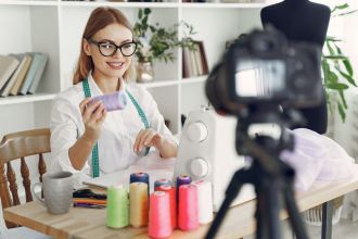 A dressmaker working at a sewing machine in her studio with a camera on a tripod beside her