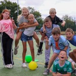 A group of children posing and pulling faces on an artificial pitch at the Phoenix Centre summer club, with coloured balls on the ground