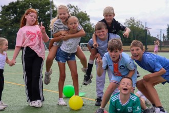 A group of children posing and pulling faces on an artificial pitch at the Phoenix Centre summer club, with coloured balls on the ground
