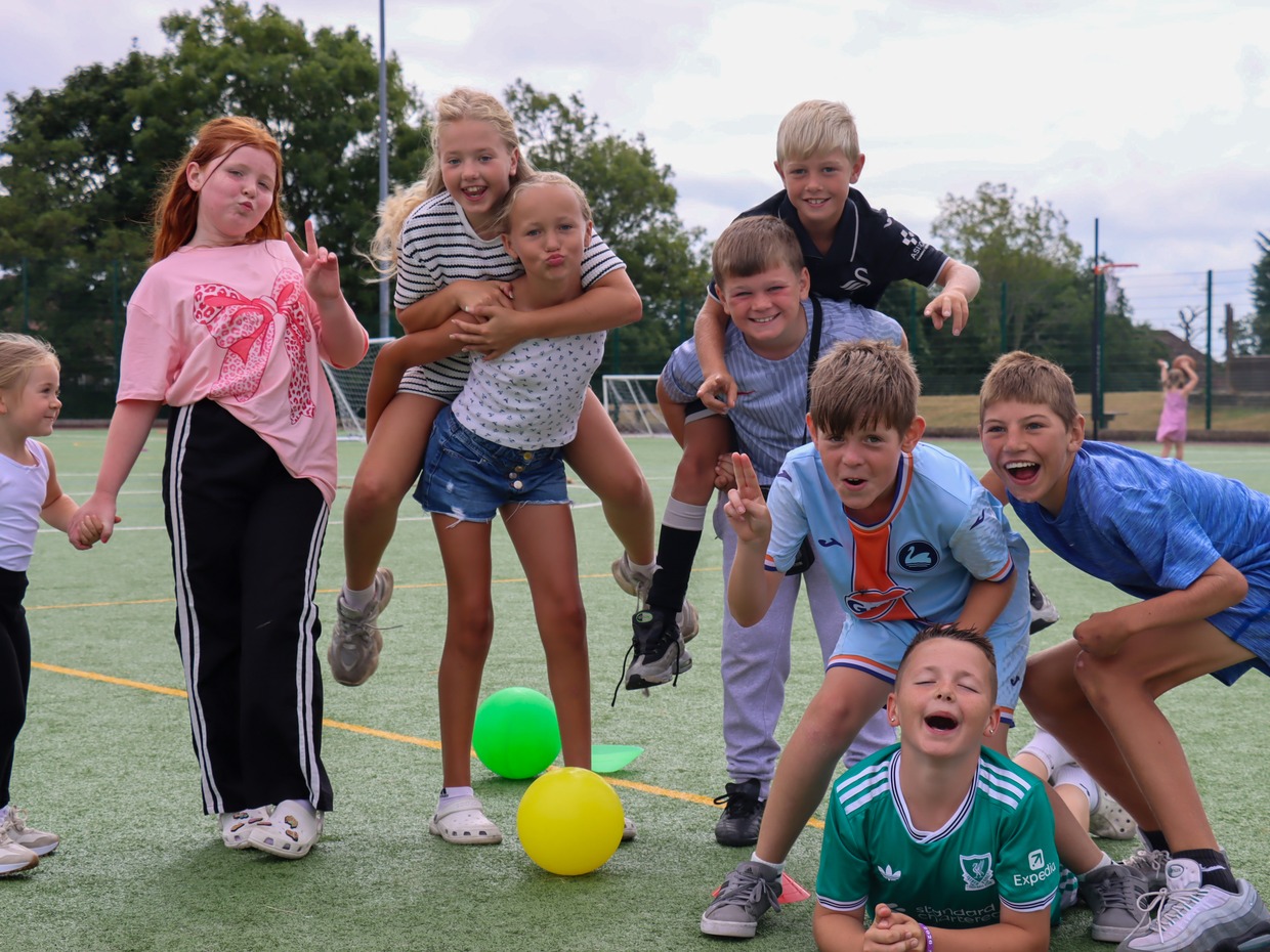 A group of children posing and pulling faces on an artificial pitch at the Phoenix Centre summer club, with coloured balls on the ground