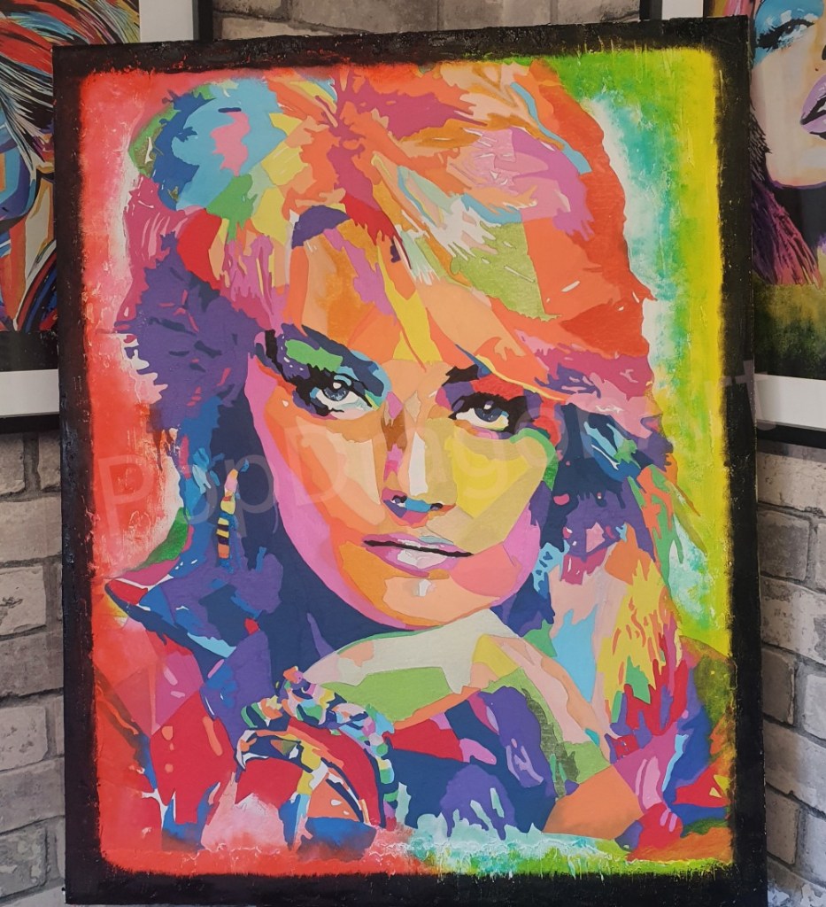 Ian Hendry's pop art portrait of Bonnie Tyler in bright blocks of colour, on a canvas leaning against a brick wall
