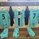 Pale blue Pure Swansea football shirts hanging on pegs in a changing room with shorts folded on the bench below