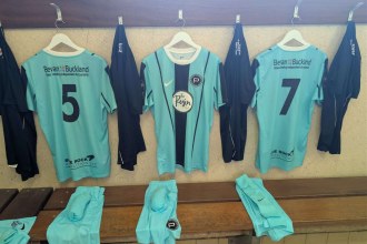 Pale blue Pure Swansea football shirts hanging on pegs in a changing room with shorts folded on the bench below