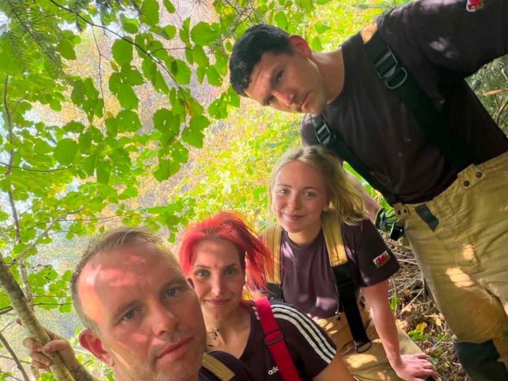 Four firefighters in soaked T-shirts and fire kit on a wooded hillside