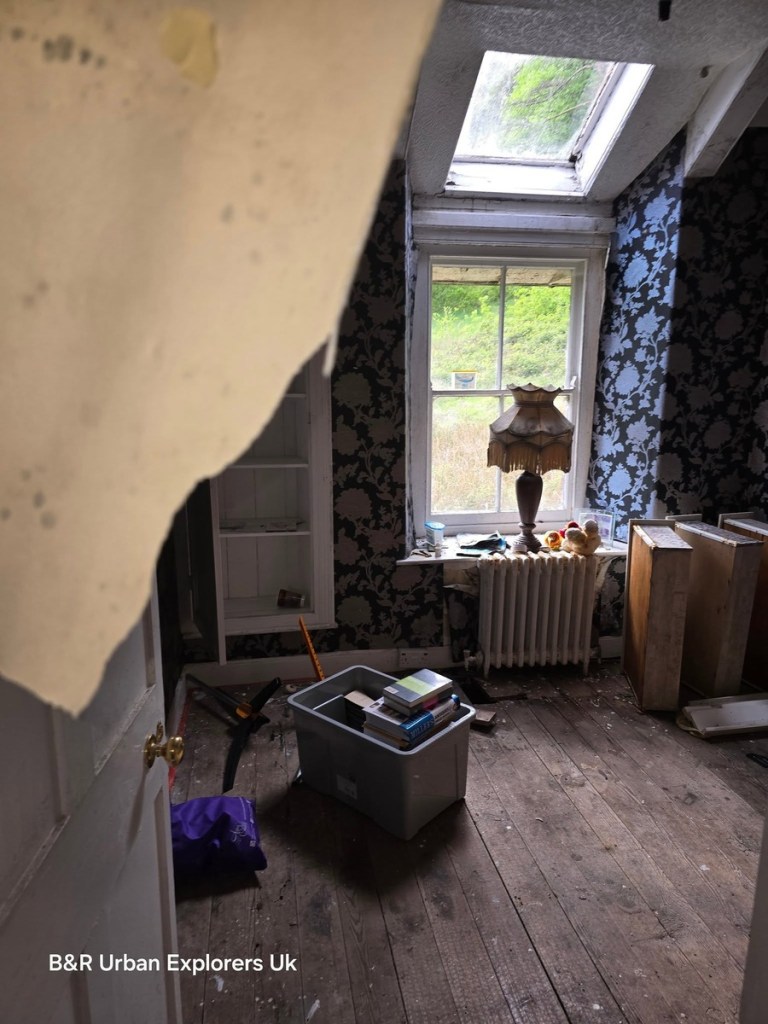 A bedroom at Rheola House with peeling floral wallpaper, a sash window and a lamp on the windowsill