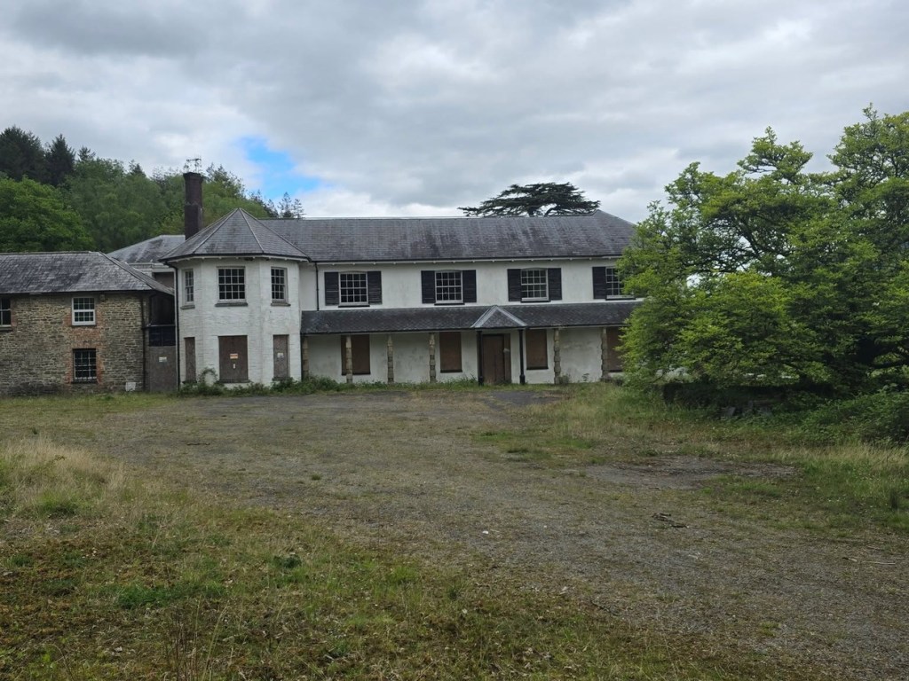 Wide view of Rheola House across a field of long grass with trees and a grey sky behind