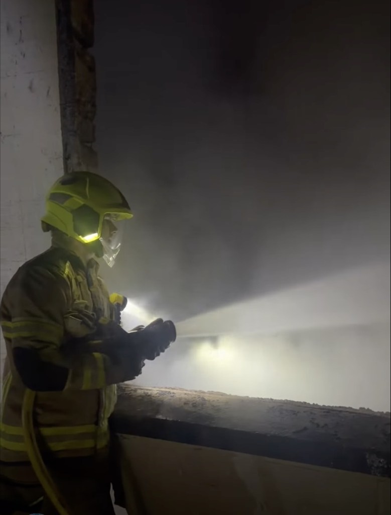A firefighter spraying a hose into a smoke-filled room inside the gutted Rheola House at night