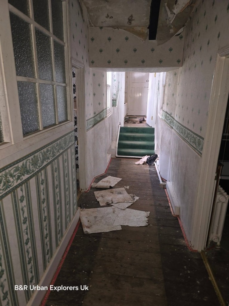 A long narrow corridor inside Rheola House with patterned wallpaper and debris on the floor