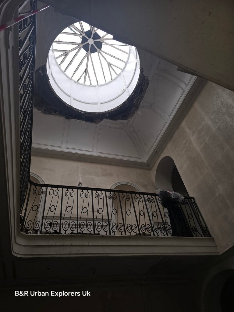 Looking up a stairwell to an oval glazed roof lantern at Rheola House, the iron balustrade curving below