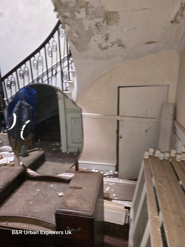 A curving staircase with iron balustrade seen from a landing inside Rheola House, a fallen mirror propped against the wall