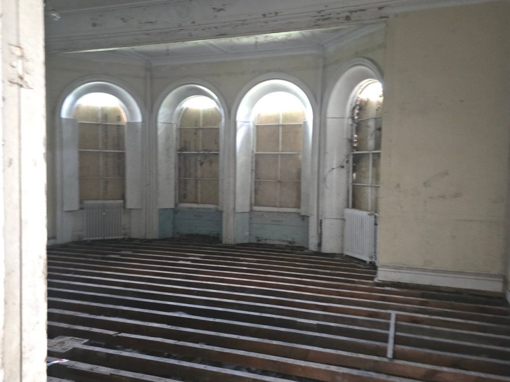 A large room inside Rheola House with stepped wooden tiers facing three tall arched windows