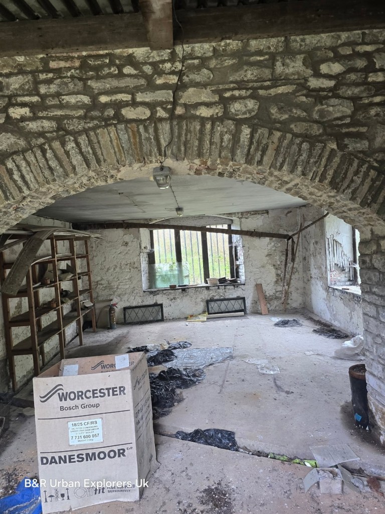 A stone-vaulted room at Rheola House with arched openings, shelving along the walls and rubbish on the floor