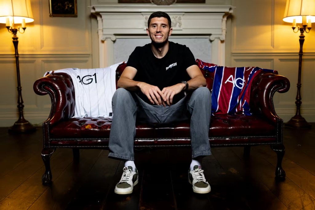 Ross Stewart sitting on a leather sofa between Swansea City's home and away shirts