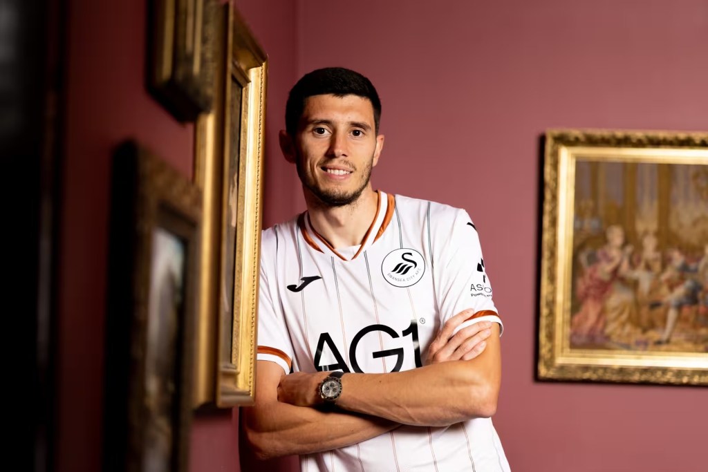 Ross Stewart in Swansea City's white and copper away shirt with his arms crossed