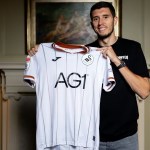 Ross Stewart holding up the white Swansea City shirt after signing for the club