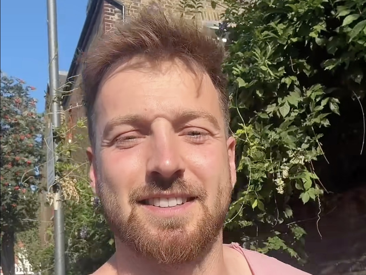 Sam Thompson smiling at the camera in a video message filmed outdoors in the sunshine
