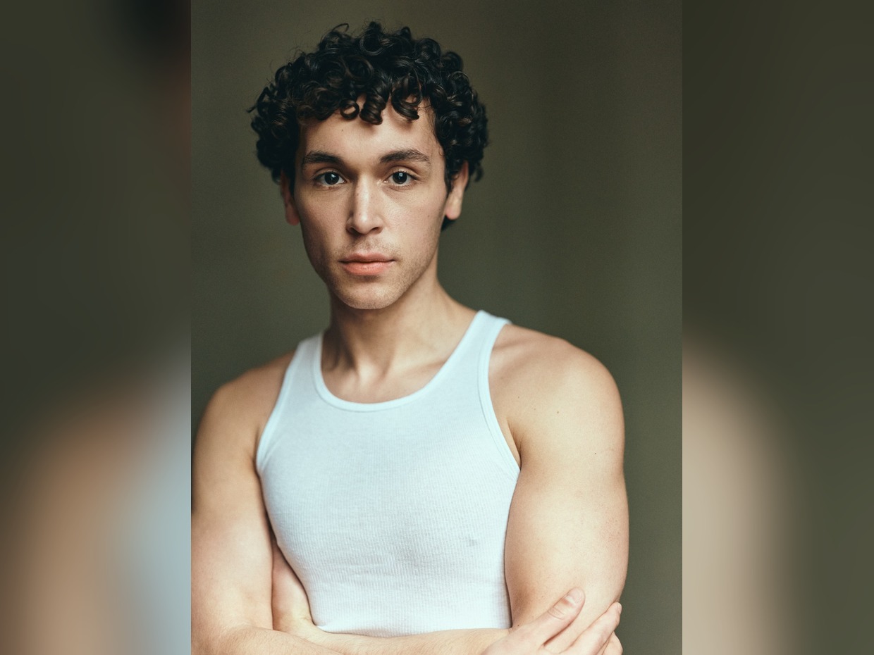 Shaheen Jafargholi in a white vest with arms folded, looking at the camera against a dark olive background