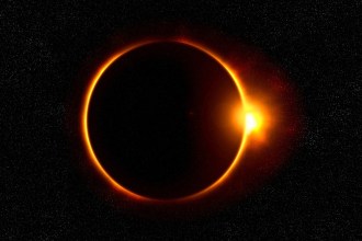 A solar eclipse showing the dark disc of the moon ringed by orange light against a starry sky, with a bright flare at its right edge