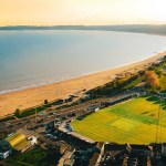Aerial view of St Helen's rugby ground beside Swansea Bay at sunset, with the beach and Mumbles headland beyond