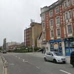A Street View image of St Helen's Road in Swansea, with the YMCA building on the right and shops lining the street