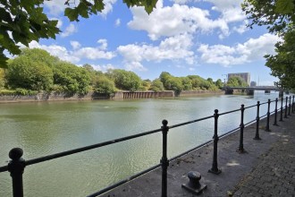 The River Tawe in Swansea seen from the western bank, with the tree-covered former railway land of the St Thomas development site opposite and the river bridges in the distance