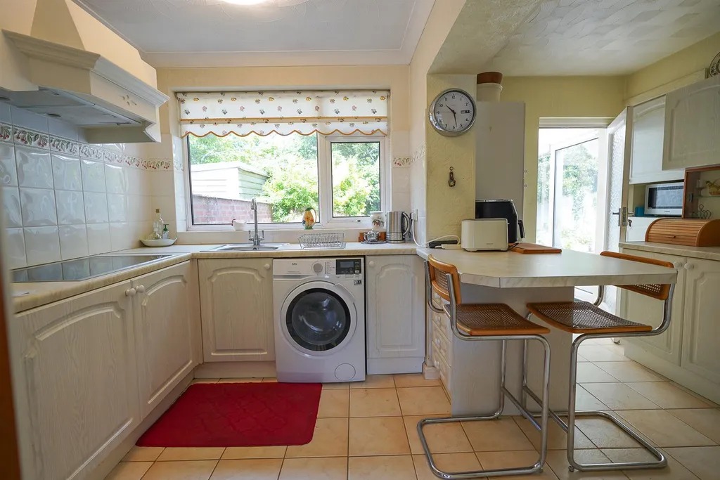 A cream fitted kitchen with a washing machine, breakfast bar and stools