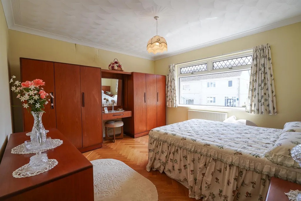 A bedroom with fitted wooden wardrobes, a dressing table and a parquet floor