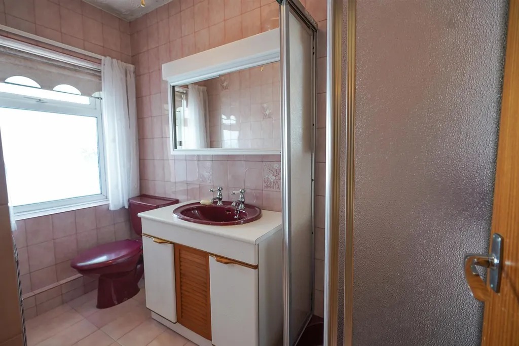 A bathroom tiled in pink with a burgundy suite and a shower cubicle