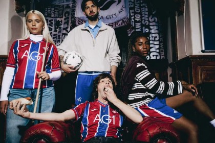 Models in the red and blue striped Swansea City 2026-27 away kit sitting in a Swansea pub with club flags behind them