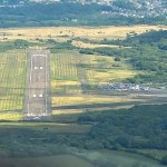 Aerial view of the single runway and apron at Swansea Airport on Fairwood Common, with hangars and parked cars alongside