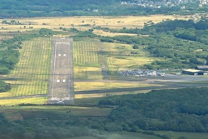 Aerial view of the single runway and apron at Swansea Airport on Fairwood Common, with hangars and parked cars alongside