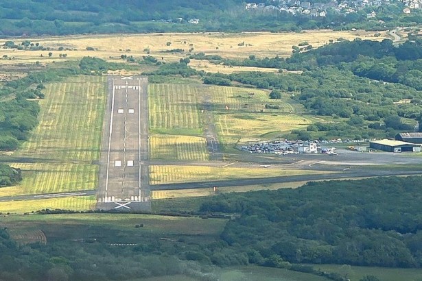 Aerial view of the single runway and apron at Swansea Airport on Fairwood Common, with hangars and parked cars alongside