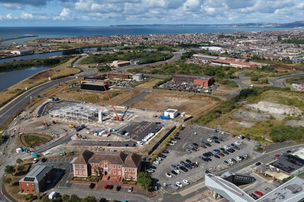 Aerial view of the SWITCH Harbourside steel frame under construction in Port Talbot, with the railway station car park and Swansea Bay behind