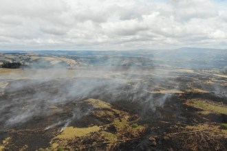 Aerial view of blackened, burnt moorland near Talley with plumes of white smoke rising and hills in the distance