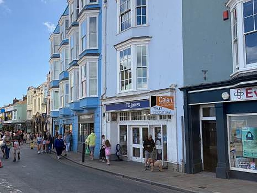 The TGJones shopfront on Tenby High Street with an orange Calan 'to let' board mounted above the fascia, shoppers passing on the pavement.