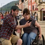Iwan Rheon and Ruth Madeley looking at a phone on a bench in Port Talbot town centre during filming of The Rapture