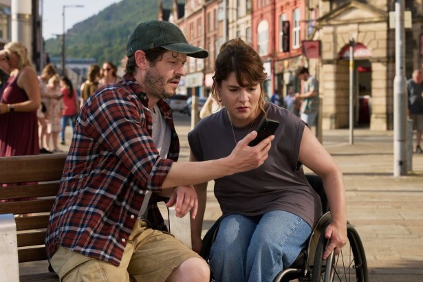 Iwan Rheon and Ruth Madeley looking at a phone on a bench in Port Talbot town centre during filming of The Rapture