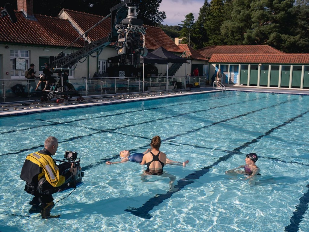 Film crew with a camera crane and an operator in the water filming a scene at an outdoor pool for The Rapture