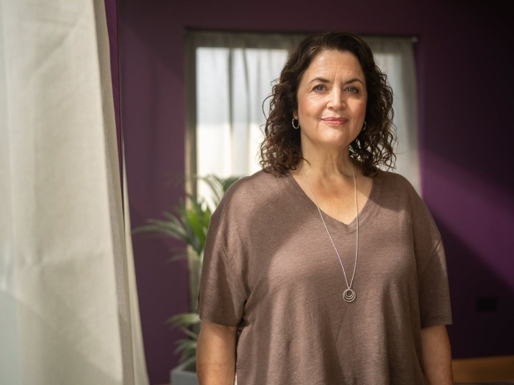 Ruth Jones standing by a window in a purple-walled room in a scene from The Rapture