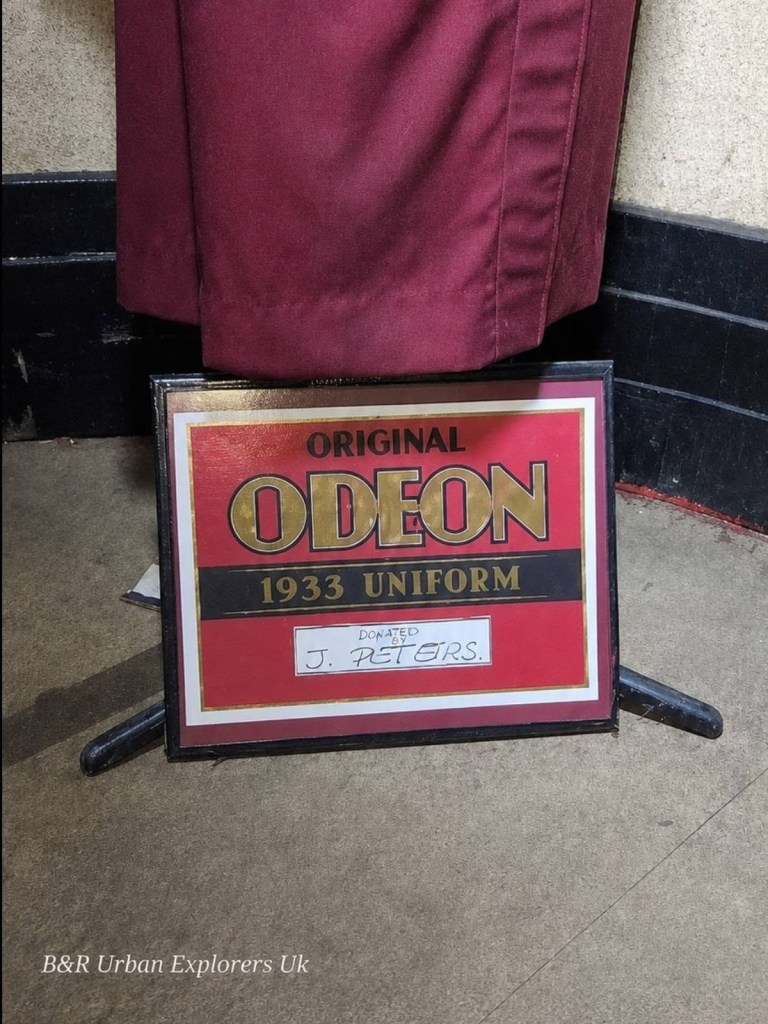 An illuminated red Odeon box sign beside a curtain inside the derelict cinema