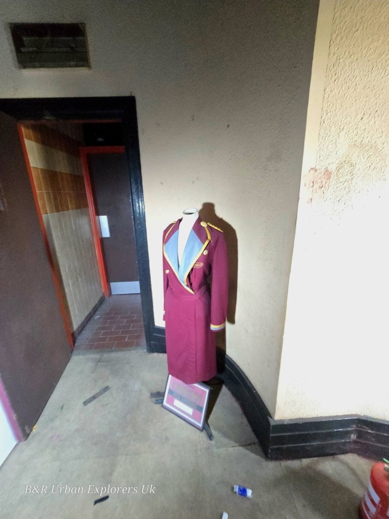 A maroon Odeon-era usher's uniform on a stand beside a doorway inside the derelict cinema