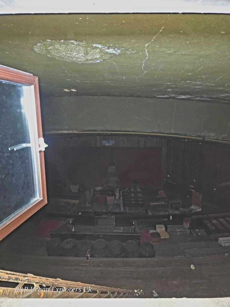 View through a small projection window down into a dark auditorium with red seats and curtains
