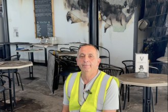 Giuseppe Cianciarulo in a hi-vis vest seated at a table inside Verdi's in Mumbles, with fire-scorched walls behind him