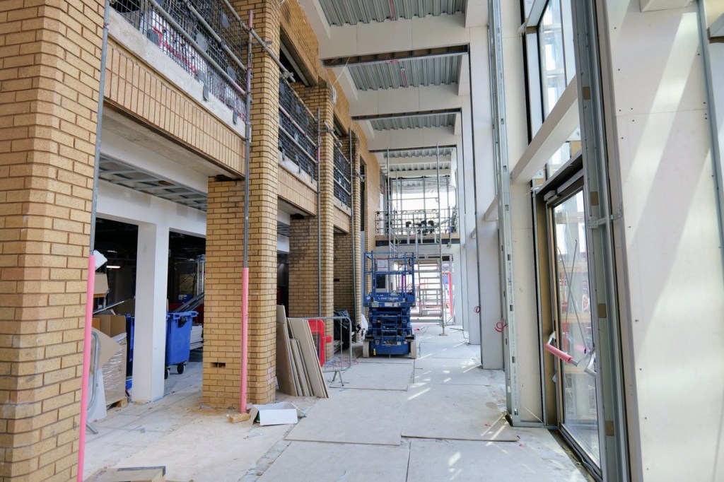 The double-height atrium foyer at Yr Aelwyd with brick columns and a scissor lift