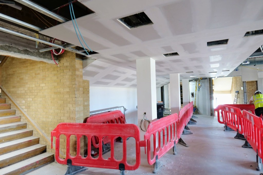 A corridor at Yr Aelwyd with red barriers, brick columns and freshly plastered ceilings