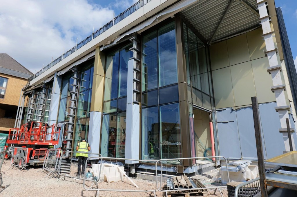 The full-height glazed frontage of Yr Aelwyd with workers and site barriers in front