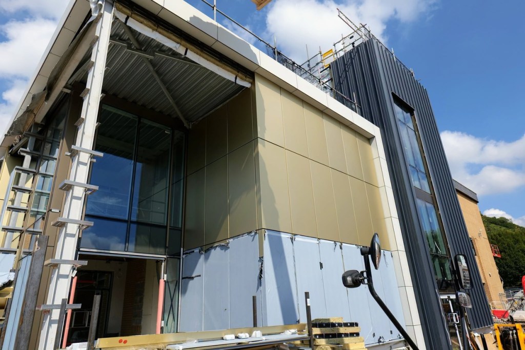 Gold cladding panels around the entrance corner of Yr Aelwyd beneath dark standing-seam cladding