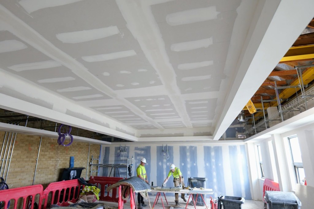 Two workers in a plastered first-floor room at Yr Aelwyd with a boxed ceiling and windows