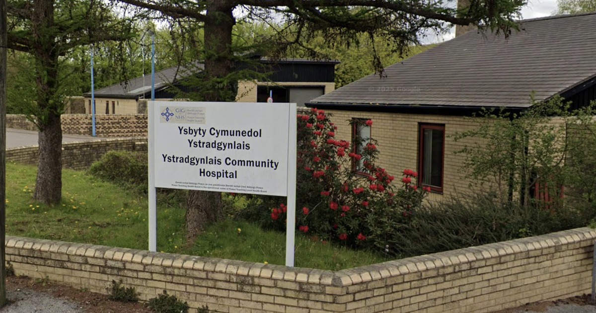The entrance sign and low brick buildings of Ystradgynlais Community Hospital, with the bilingual Ysbyty Cymunedol Ystradgynlais sign in front