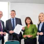 Four party representatives stand together in Cardiff with a copy of the agreement held up.